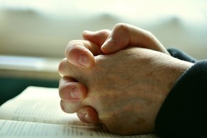 folded hands resting on a Bible